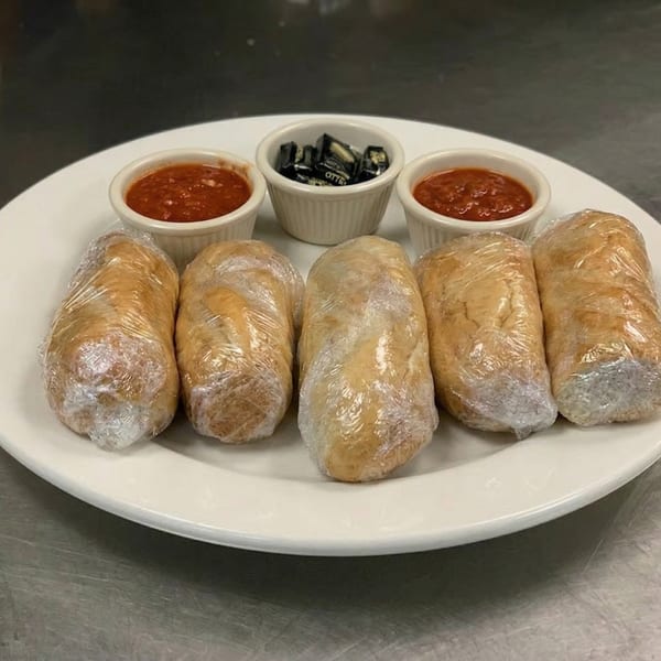 Five wrapped dough rolls on a white plate with two small bowls of marinara and one of candies.