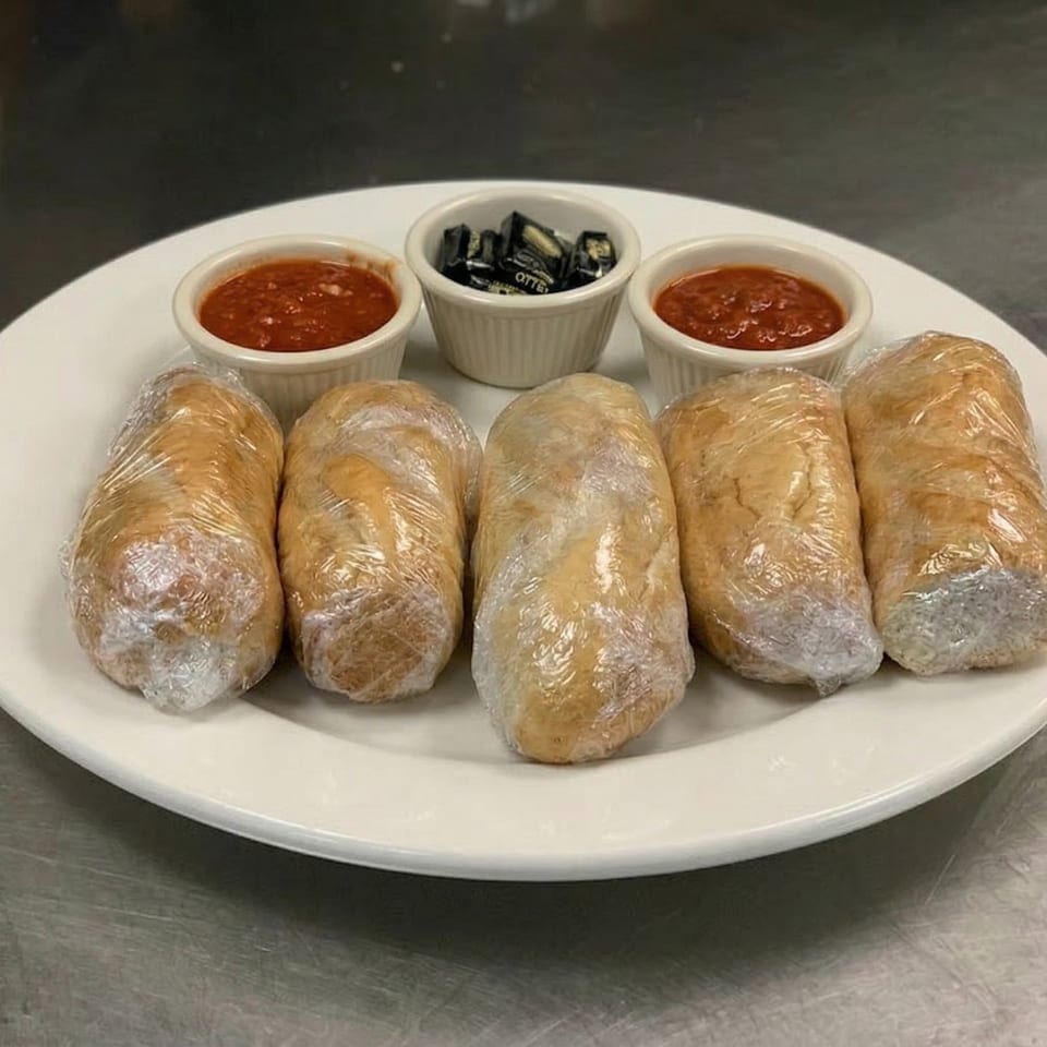 Five wrapped dough rolls on a white plate with two small bowls of marinara and one of candies.