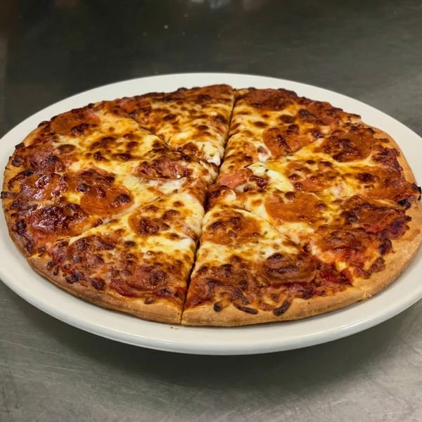 A whole pepperoni pizza, cut into slices, on a white plate against a dark background.