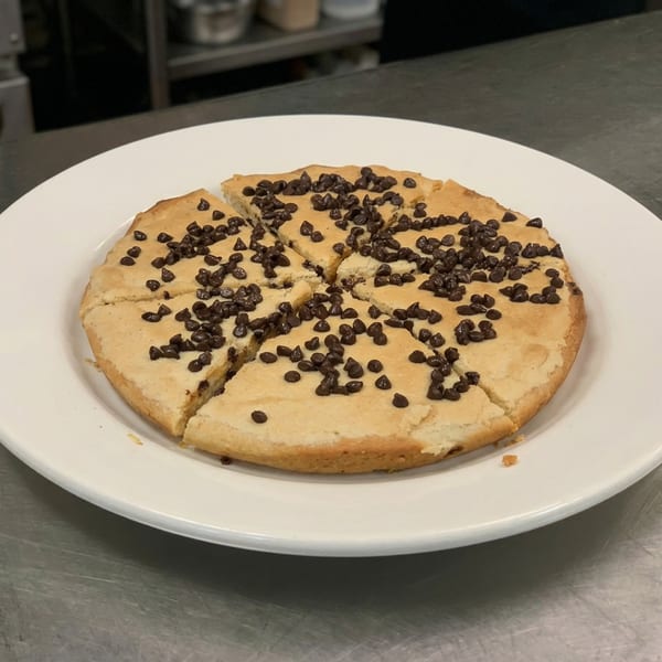 A round, sliced cookie cake topped with chocolate chips on a white plate.
