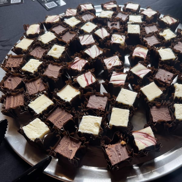 A silver tray filled with rows of mini cheesecakes in chocolate cups, some plain, some swirled.