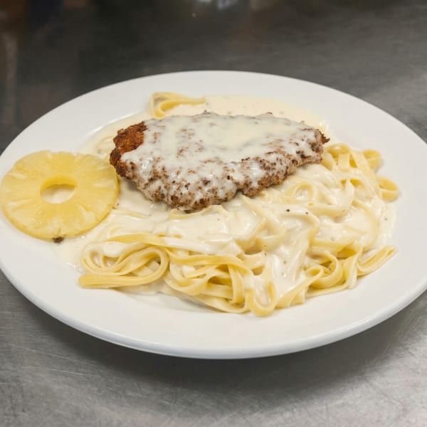Breaded chicken cutlet with melted cheese, fettuccine alfredo, and a pineapple ring on a white plate.