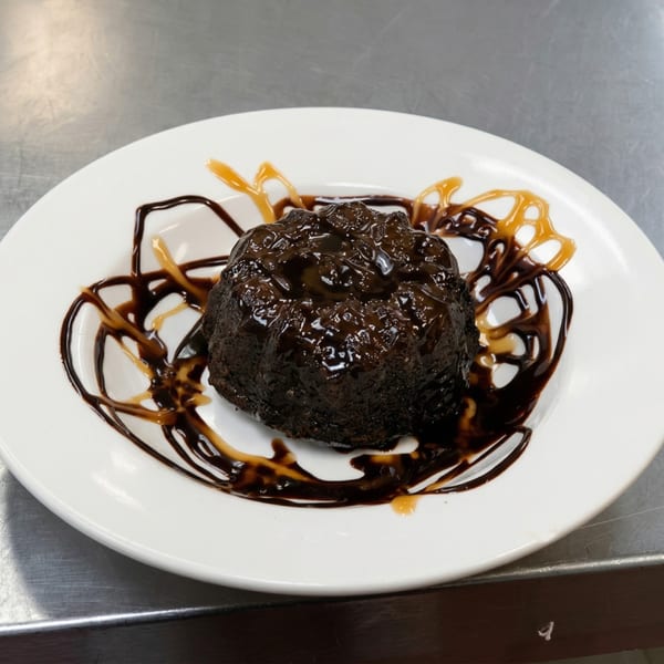 A rich chocolate lava cake, drizzled with chocolate and caramel sauce, on a white plate.